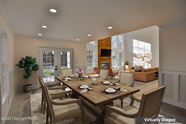 dining room with french doors, a wainscoted wall, crown molding, a stone fireplace, and a decorative wall