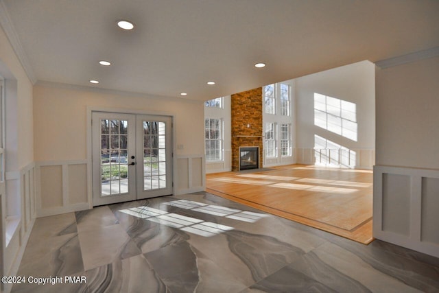 unfurnished living room featuring french doors, crown molding, a fireplace, a decorative wall, and wainscoting