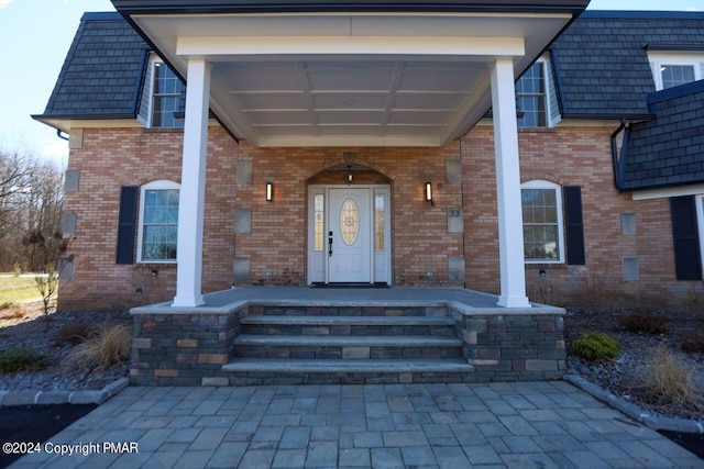 view of exterior entry with a porch, brick siding, and mansard roof