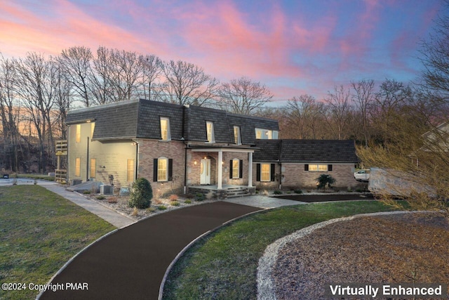 view of front of house with a front yard, central AC unit, mansard roof, and brick siding