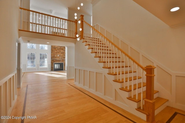 staircase featuring a stone fireplace, recessed lighting, a decorative wall, wood finished floors, and a towering ceiling