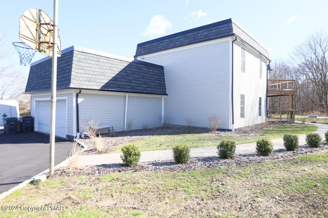 view of home's exterior featuring an attached garage, aphalt driveway, mansard roof, and a lawn