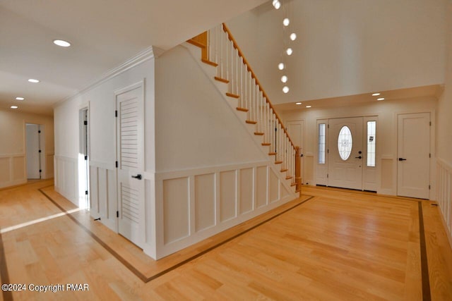 foyer entrance with recessed lighting, a decorative wall, ornamental molding, wood finished floors, and stairs