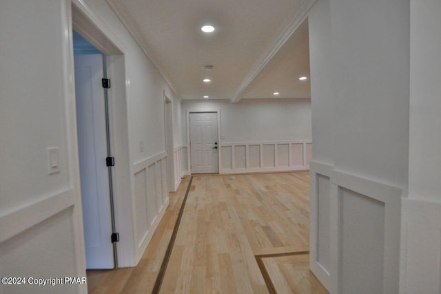 hallway with light wood finished floors, a wainscoted wall, crown molding, a decorative wall, and recessed lighting