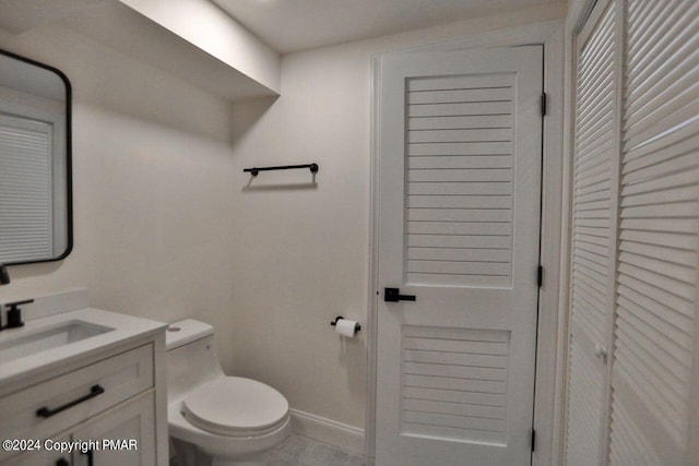 bathroom featuring toilet, baseboards, a closet, and vanity