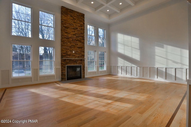 unfurnished living room featuring a stone fireplace, a high ceiling, coffered ceiling, wood finished floors, and beamed ceiling