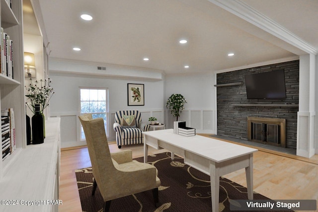 office space featuring a wainscoted wall, crown molding, light wood-style floors, a fireplace, and a decorative wall