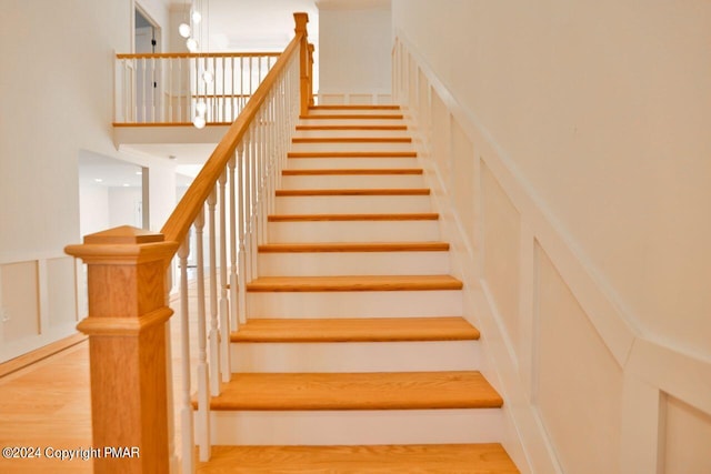 stairway featuring a decorative wall, a towering ceiling, and wood finished floors