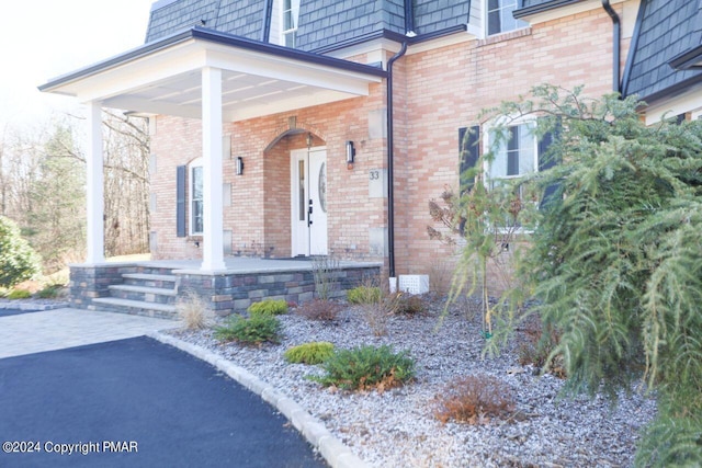 doorway to property featuring covered porch, brick siding, and mansard roof