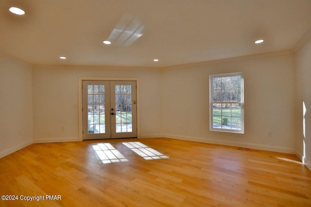 empty room featuring light wood finished floors, baseboards, ornamental molding, and french doors