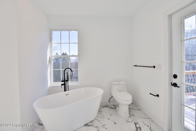 bathroom featuring marble finish floor, a freestanding tub, toilet, and baseboards