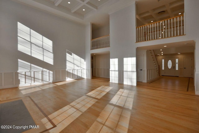 unfurnished living room featuring beam ceiling, a high ceiling, coffered ceiling, and wood finished floors