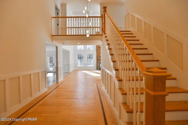 stairway featuring french doors, a wainscoted wall, a decorative wall, a towering ceiling, and wood finished floors