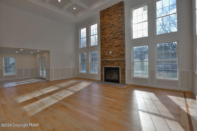 unfurnished living room with beam ceiling, a decorative wall, a stone fireplace, wood finished floors, and coffered ceiling