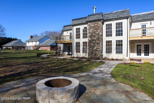 rear view of house featuring french doors, mansard roof, a lawn, a balcony, and a fire pit