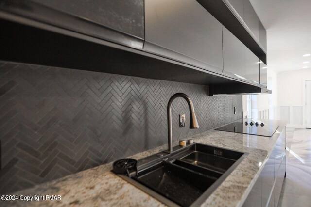 kitchen with light stone counters, a sink, backsplash, and black electric cooktop