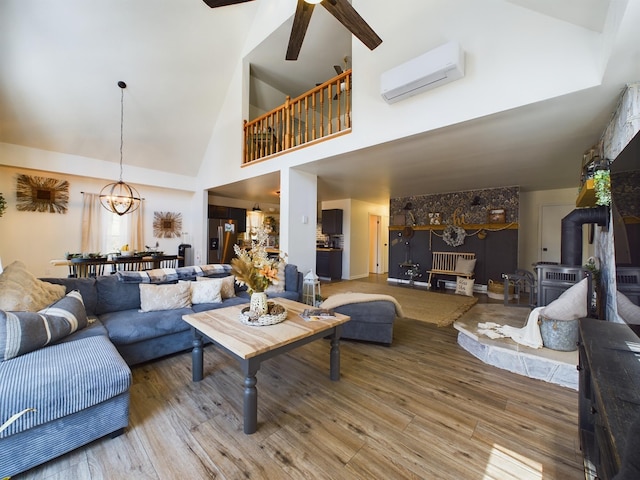 living room featuring high vaulted ceiling, an AC wall unit, ceiling fan with notable chandelier, wood finished floors, and a wood stove