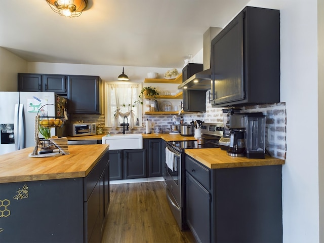 kitchen featuring wall chimney range hood, butcher block counters, a sink, and appliances with stainless steel finishes