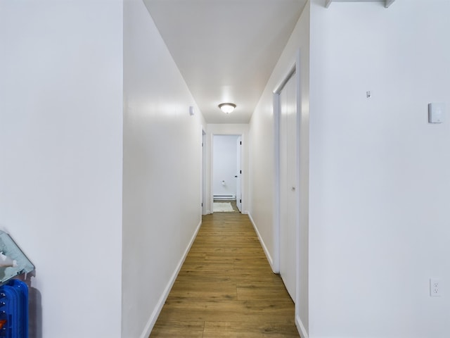 hallway featuring baseboards, baseboard heating, and wood finished floors