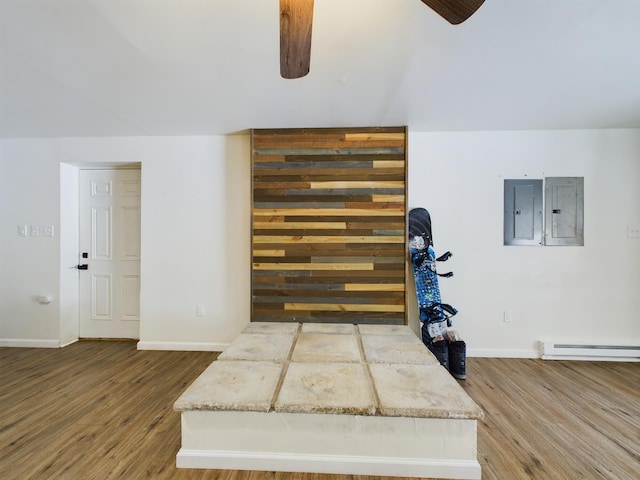 bonus room with a baseboard heating unit, ceiling fan, wood finished floors, and electric panel