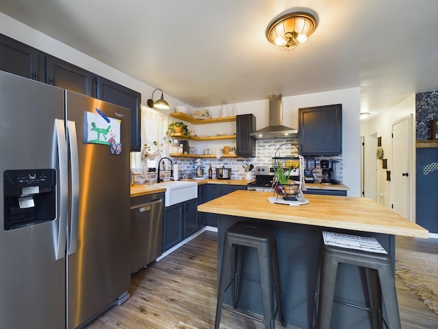 kitchen featuring a breakfast bar area, stainless steel appliances, butcher block counters, a sink, and wall chimney exhaust hood