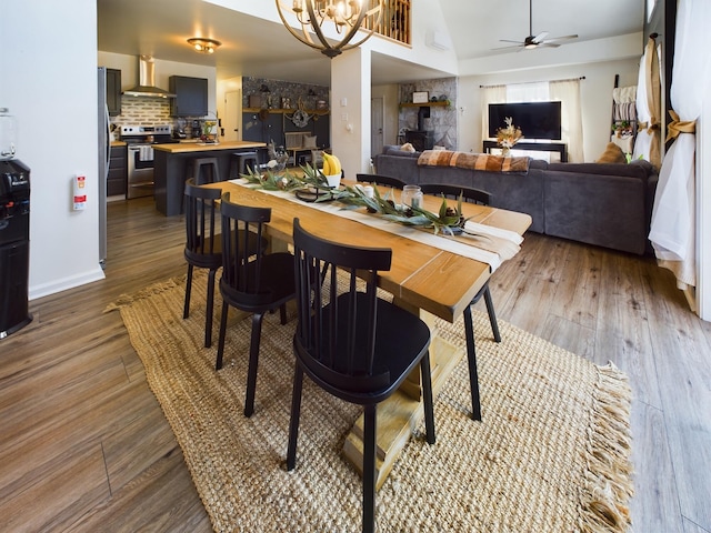 dining room featuring lofted ceiling, a stone fireplace, wood finished floors, and ceiling fan with notable chandelier