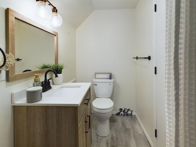 full bathroom featuring toilet, wood finished floors, vanity, baseboards, and vaulted ceiling