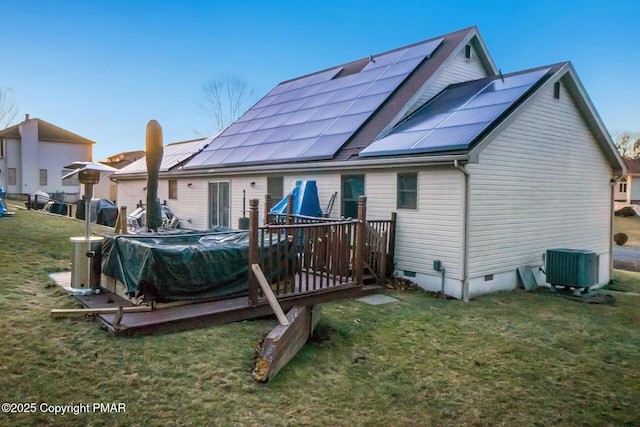 rear view of house with a yard, a wooden deck, solar panels, and central air condition unit