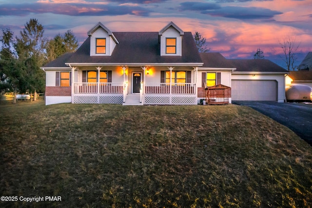 cape cod-style house with a porch, an attached garage, aphalt driveway, a lawn, and brick siding