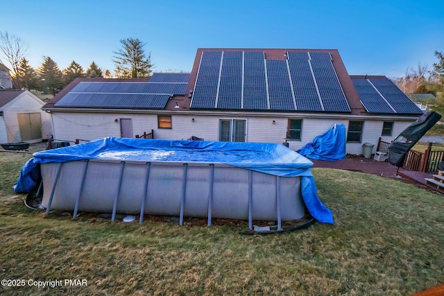 back of house with a covered pool, solar panels, and a lawn