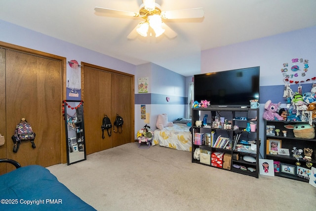 bedroom featuring light carpet, ceiling fan, and multiple closets