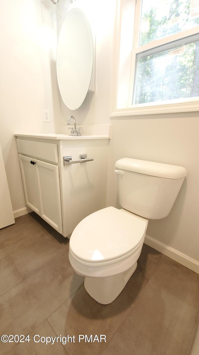 half bath with toilet, vanity, baseboards, and tile patterned floors