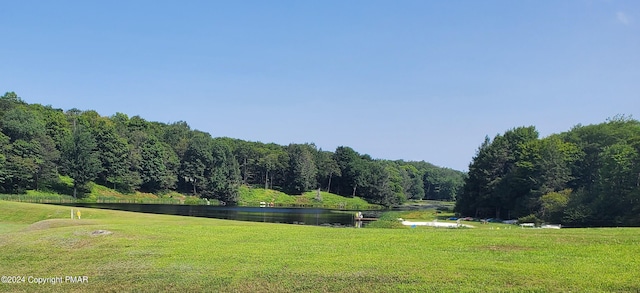 view of property's community featuring a lawn, a water view, and a wooded view