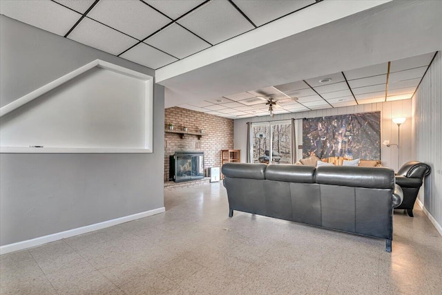 living room with a drop ceiling, baseboards, and a brick fireplace