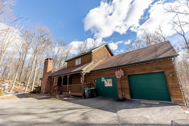 view of front of property with a garage, a chimney, aphalt driveway, roof with shingles, and a porch