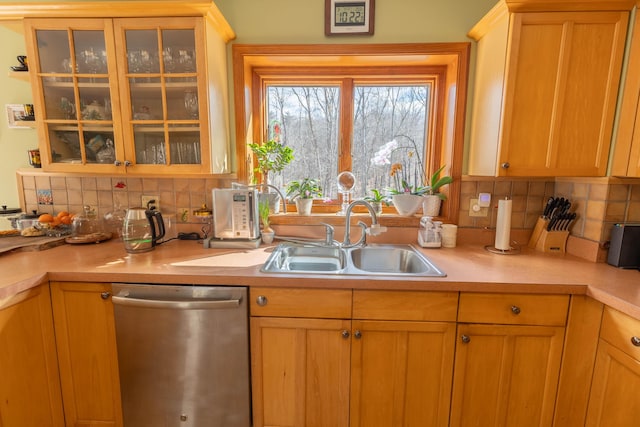 kitchen featuring light countertops, stainless steel dishwasher, a sink, and tasteful backsplash