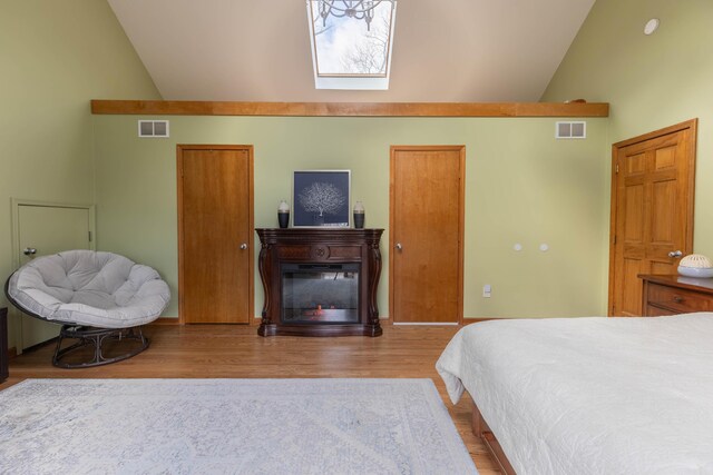 bedroom featuring high vaulted ceiling, visible vents, wood finished floors, and a glass covered fireplace