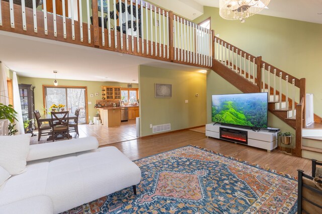 living area with visible vents, a high ceiling, an inviting chandelier, wood finished floors, and stairs