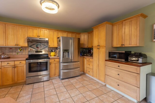 kitchen with appliances with stainless steel finishes, light tile patterned flooring, backsplash, and under cabinet range hood