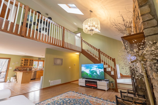 living room featuring a skylight, visible vents, stairway, wood finished floors, and a high ceiling