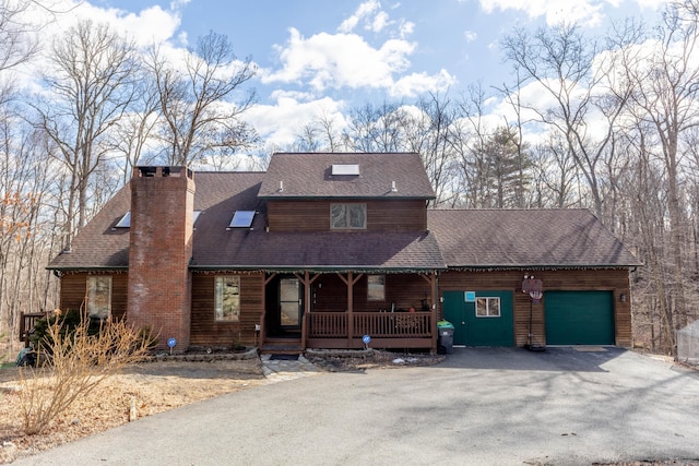 chalet / cabin with roof with shingles, a chimney, a porch, an attached garage, and driveway