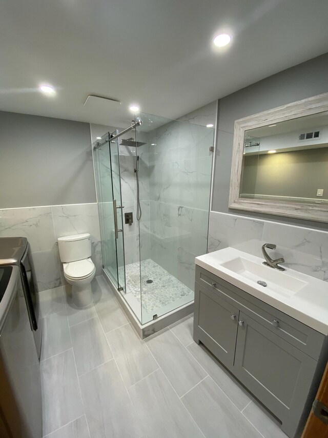 full bath featuring toilet, vanity, visible vents, a marble finish shower, and washer and clothes dryer