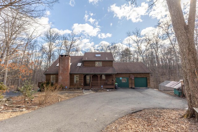 view of front of home with driveway, covered porch, a garage, and a chimney