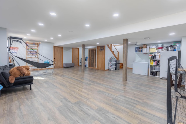 finished basement featuring stairs, wood finished floors, freestanding refrigerator, and recessed lighting