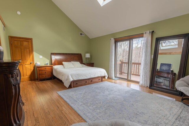 bedroom featuring a skylight, visible vents, wood finished floors, access to outside, and high vaulted ceiling