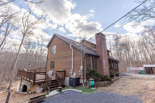 view of side of home featuring roof with shingles, a chimney, a wooden deck, and central air condition unit