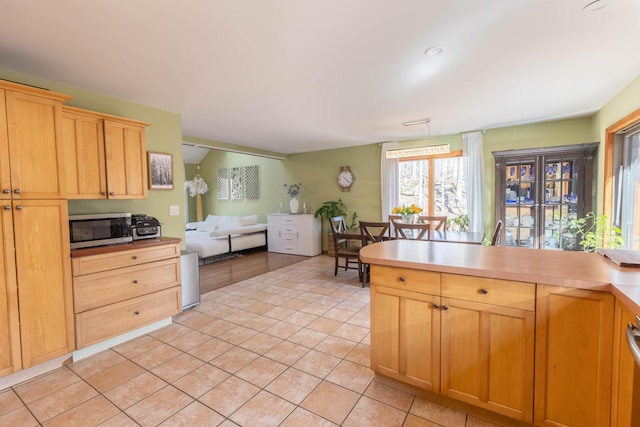 kitchen featuring stainless steel microwave, open floor plan, light countertops, light brown cabinets, and light tile patterned flooring