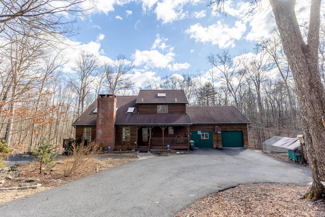 rustic home with a garage, covered porch, a chimney, and aphalt driveway