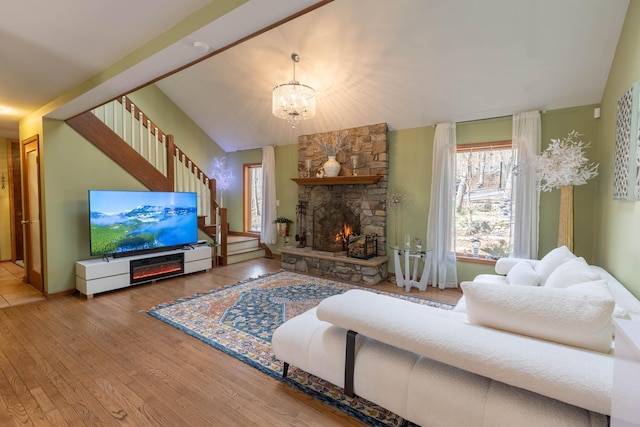 living area with a notable chandelier, a fireplace, wood finished floors, stairs, and vaulted ceiling