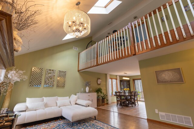 living room featuring a skylight, visible vents, a chandelier, wood finished floors, and high vaulted ceiling